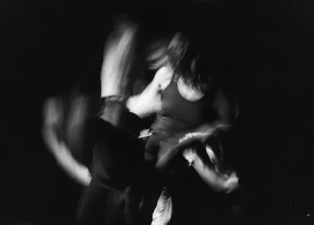 Niewyraźne, rozmazane zdjęcie. Aktorka w czarnej koszulce na ramiączka oraz ktoś stojący obok niej wykonuje ekspresyjne ruchy.