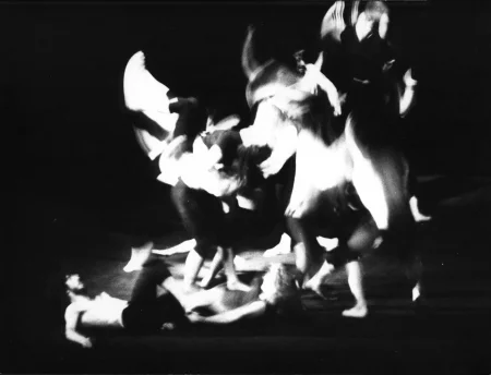 Niewyraźne, rozmazane zdjęcie. Grupa aktorów w ekspresyjnych, akrobatycznych pozach. Po lewej stronie na scenie w bezruchu leży dwoje aktorów.