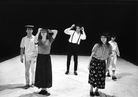 Pięcioosoba grupa aktorów i aktorek stoi na białej płachcie zwrócona twarzą w stronę widza. Każdy ma czarne nakrycie głowy.