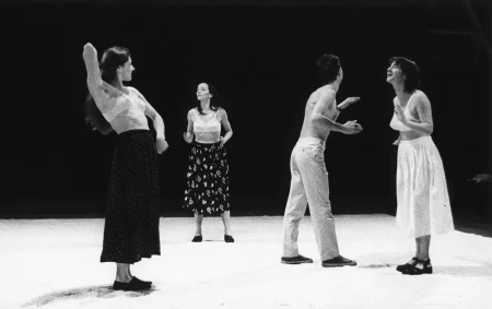 Na scenie stoją trzy aktorki i jeden aktor. Aktorki ubrane są w spódnice i staniki. Aktor jest ubrany w jasne spodnie i ma nagi tors. Wszyscy gestykulują dłońmi.