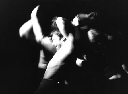 Niewyraźne, rozmazane zdjęcie. Aktor bez koszulki stoi zwrócony do nas profilem. Wygląda na zmęczonego. Za jego plecami grupa aktorów wykonuje ekspresyjne ruchy.