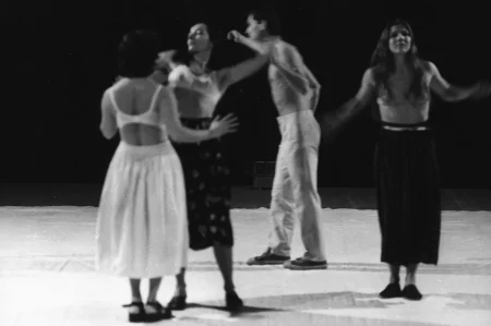Niewyraźne zdjęcie. Na białej płachcie stoją trzy aktorki i jeden aktor. Aktorki ubrane są w spódnice i staniki. Aktor jest ubrany w jasne spodnie i ma nagi tors. Wszyscy wyglądają, jakby tańczyli.