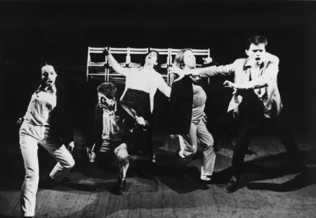 Przestrzeń miejska. Między budynkami stoi tłum ludzi zwróconych plecami w stronę widza. Niektórzy trzymają w rękach białe flagi.