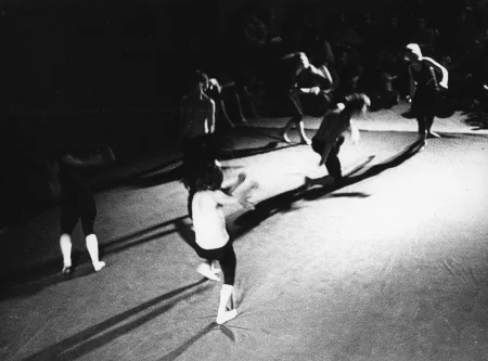 Scena wyglądająca jak wyłożona prześcieradłem. Na scenie grupa aktorów i aktorek widzianych od góry.Stoją oddzielnie wykonując bardzo ekspresyjne ruchy. Na drugim planie siedząca grupa widzów.