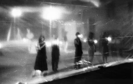 Niewyraźne zdjęcie. Grupa aktorów i aktorek stoi w szeregu za przeźroczystą płachtą. W rękach trzymają latarki.