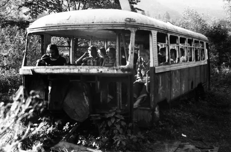 Stary, zniszczony autobus w środku lasu. W środku autobusu siedzą aktorzy. Ubrani są prywatnie, wyglądają jakby byli pasażerami.