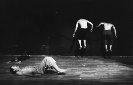 Po lewej stronie na brzuchu leży aktorka. Ubrana jest w czarne spodenki i czarną podkoszulkę. Patrzy w stronę widza. W centrum, na pierwszym planie na plecach leży aktor.Ubrany jest w jasne spodenki, ma nagi tors. Ma oderwane stopy od ziemi i ugięte nogi. Po prawej stronie, tyłem do widza skacze w miejscu dwóch aktorów. Ubrani są w ciemne spodenki, mają nagie torsy.