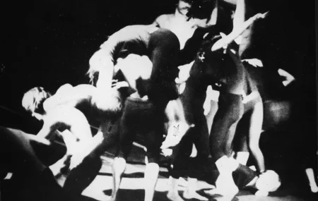 Niewyraźna grupa aktorów w akobatycznych pozach. Wszyscy są boso i stoją na czarno-białej podłodze.