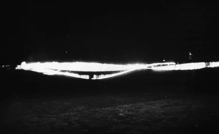 Niewyraźne zdjęcie. Na brukowanej ulicy stoją aktorzy. Trzymają przedmioty emitujące silne światło.