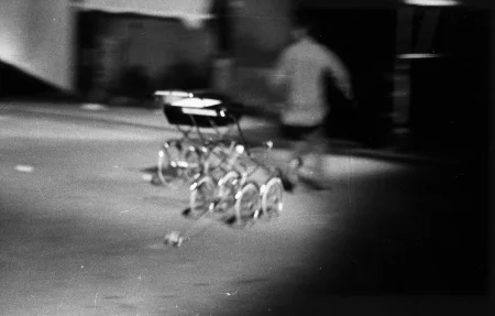 Niewyraźne zdjęcie. Dwa wózki dziecięce. W tle przechodzi osoba odwrócona plecami do widza.