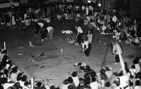 Przestrzeń miejska. Z góry widać aktorów pośród publiczności. Poza aktorami na scenie znajdują się zabawki, takie jak samochodzik, lalka czy wózek z koniem.