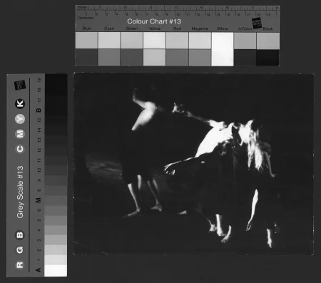 Niewyraźne, rozmazane zdjęcie. Troje aktorów stoi jeden za drugim. Każdy aktor trzyma za głowę aktora stojącego obok niego. Aktor stojący w głębi sceny jest zwrócony do nas plecami. Aktor stojący pośrodku wygina się, jakby chciał isć w głąb sceny. Za głowę trzyma go aktorka zwrócona do nas przodem.