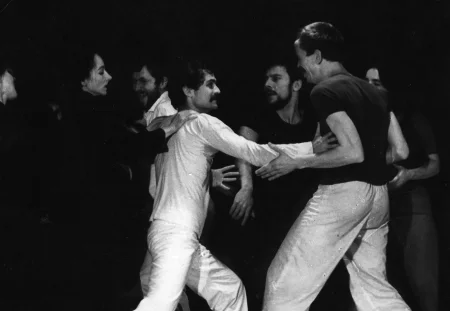 Grupa aktorów i aktorek w bliskim kontakcie fizycznym. Energicznie się ruszają. Niektórzy są poważni, inni się śmieją. Dwóch aktorów w centrum wygląda, jakby mieli się bić.