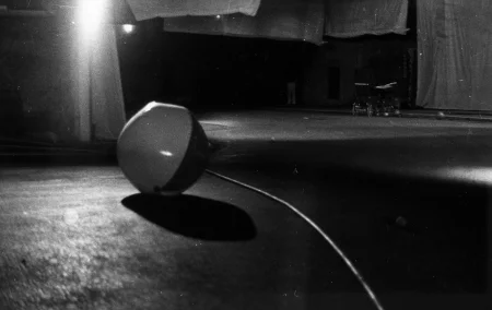 Czarno-biała piłka rzuca cień na podłogę. W oddali stoją dwa dziecięce wózki i ledwo widoczna osoba zwrócona do widza plecami.