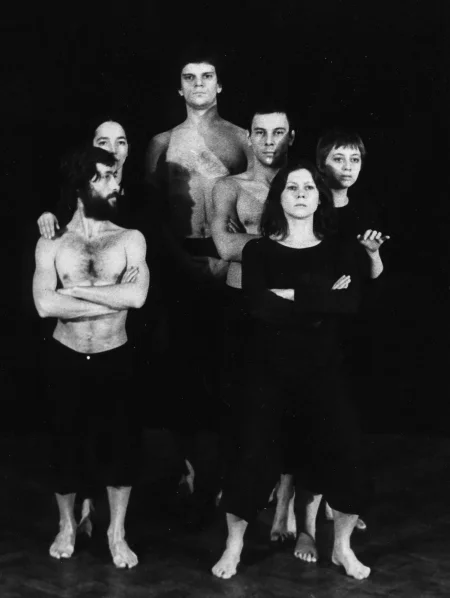 Grupa aktorów i aktorek stojących twarzą w stronę widza. Wyglądają, jakby pozowali do zdjęcia. Aktor i aktorka z przodu napinają mięśnie. Aktor jako jedyny patrzy w bok. Jest ubrany w czarne spodenki i ma nagi tors. Aktorka ubrana jest w czarne sodnie i czarnę koszulkę. Za nimi stoją dwie aktorki i jeden aktor. Z tyłu stoi bardzo wysoki aktor.