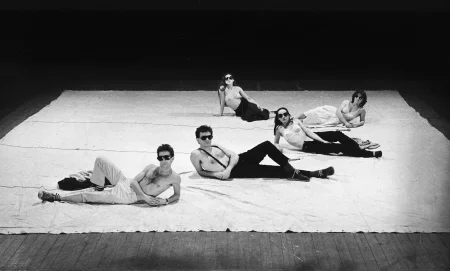 Pięcioosobowa grupa aktorów i aktorek leży na białej płachcie. Wyglądają, jakby pozowali do zdjęcia. Aktorzy mają nagie torsy, aktorki mają na sobie staniki. Wszyscy noszą ciemne okulary przeciwsłoneczne.