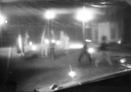 Niewyraźne zdjęcie. Grupa aktorów stoi za przeźroczystą płachtą.