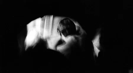 Niewyraźne, rozmazane zdjęcie. Aktor stoi zwrócony do nas tyłem. Jest lekko pochylony do przodu.