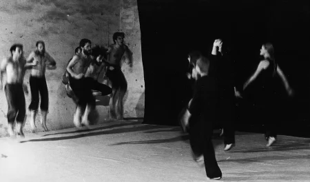 Po dwóch stronach sceny, na tle czarnej płachty, stoją aktorzy i aktorki. Aktorzy po lewej stronie, aktorki po prawej. Obie grupy są zwrócone w swoją stronę. Aktorzy ubrani są w czarne spodenki, mają nagie torsy. Aktorki ubrane są w czarne spodnie i czarne koszulki. Obie grupy podskakują.