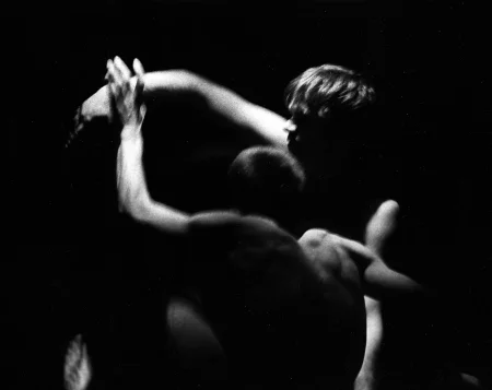 Dwóch aktorów stoi blisko siebie. Mają nagie torsy. Obaj mają wyciągniętą przed siebie jedną rękę. Ich wyciągnięte ręce wyglądają, jakby się lekko stykały.