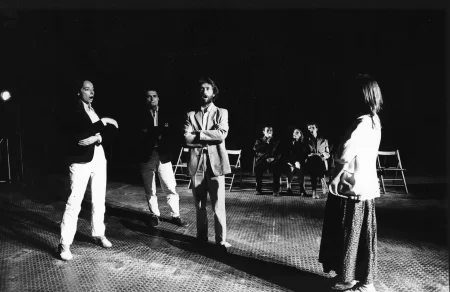 Niewyraźne zdjęcie. Przestrzeń miejska. Między budynkami stoi tłum ludzi. Niektórzy trzymają w rękach białe flagi. W stronę tłumu podchodzi ekipa filmowa.