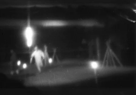 Niewyraźne zdjęcie. W oddali widać biegnącego aktora i kilka świecących reflektorów.