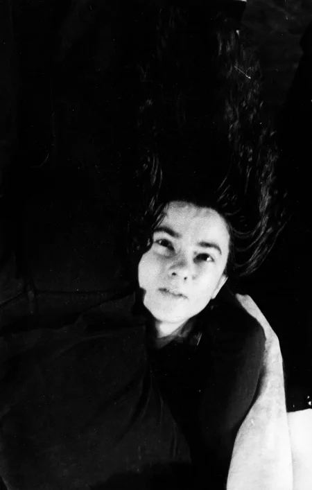 Aktorka, ubrana na czarno, zwisa głową w dół. Ma skupioną twarz i patrzy w naszym kierunku. Jej długie falowane włosy zwisają na podłogę.