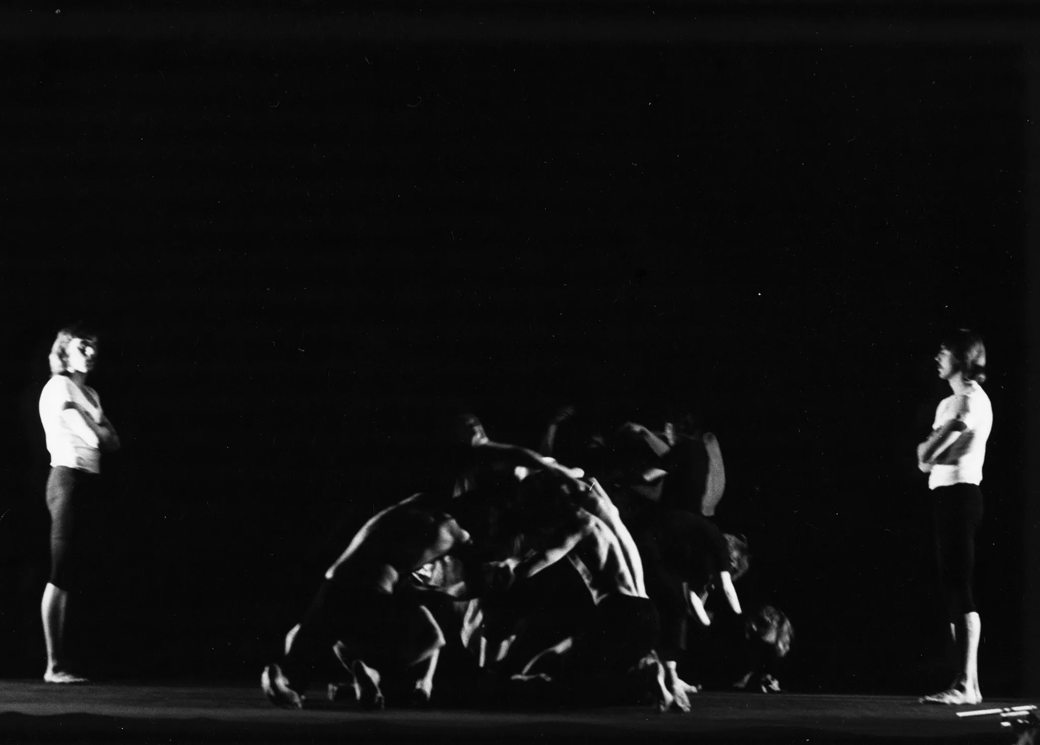 W centrum grupa aktorów w akboratycznych pozach. Na pierwszym planie dwóch wysportowanych mężczyzn bez koszulek trzyma się wzajemnie tworząc okrąg. Po lewej i prawej stronie stoi jeden aktor w białym podkoszulku i czarnych spodenkach. Obaj patrzą grupę aktorów w centrum.