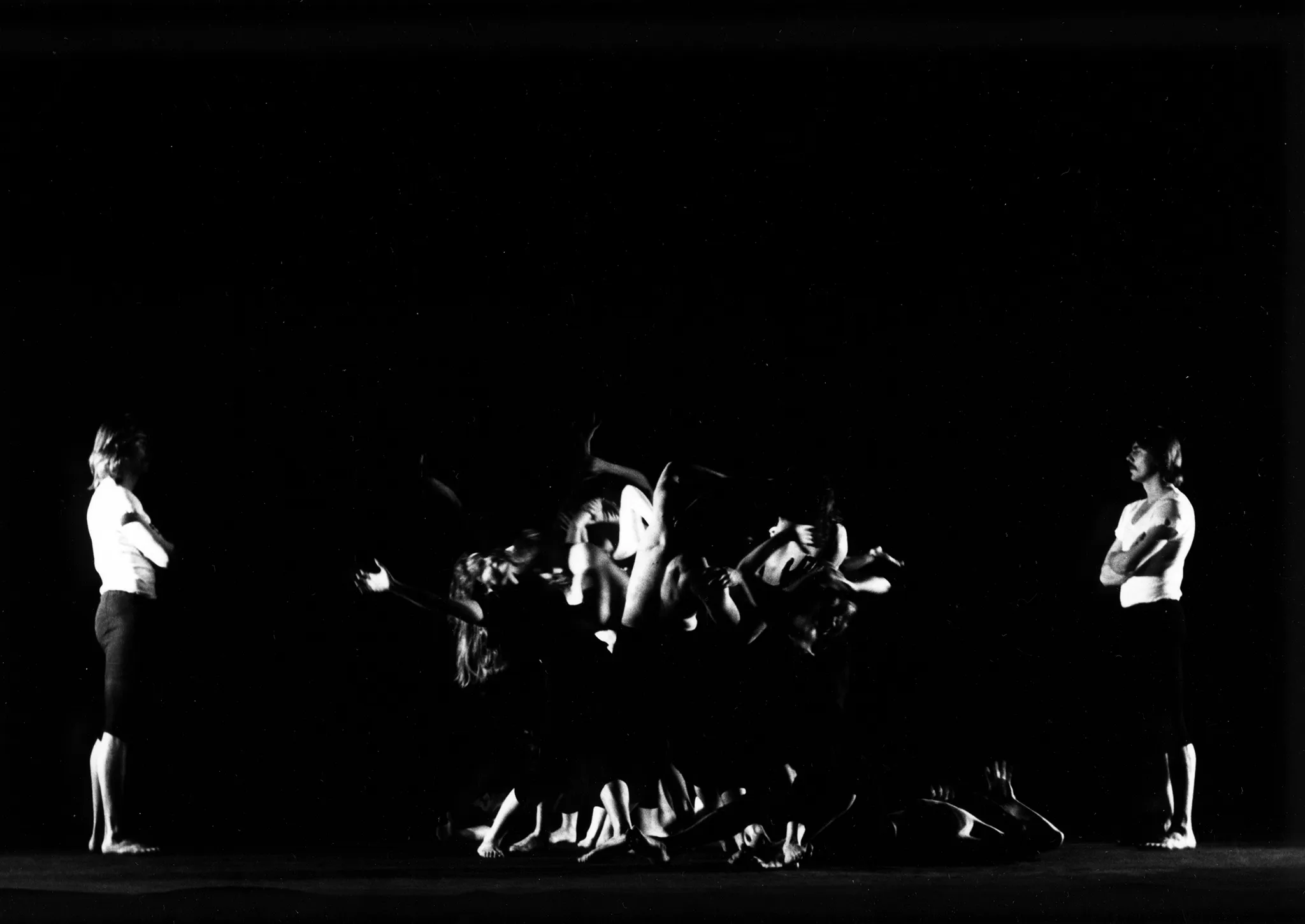 W centrum grupa aktorów w akboratycznych pozach. Na pierwszym planie dwóch wysportowanych mężczyzn bez koszulek trzyma się wzajemnie tworząc okrąg. Po lewej i prawej stronie stoi jeden aktor w białym podkoszulku i czarnych spodenkach. Obaj patrzą grupę aktorów w centrum.