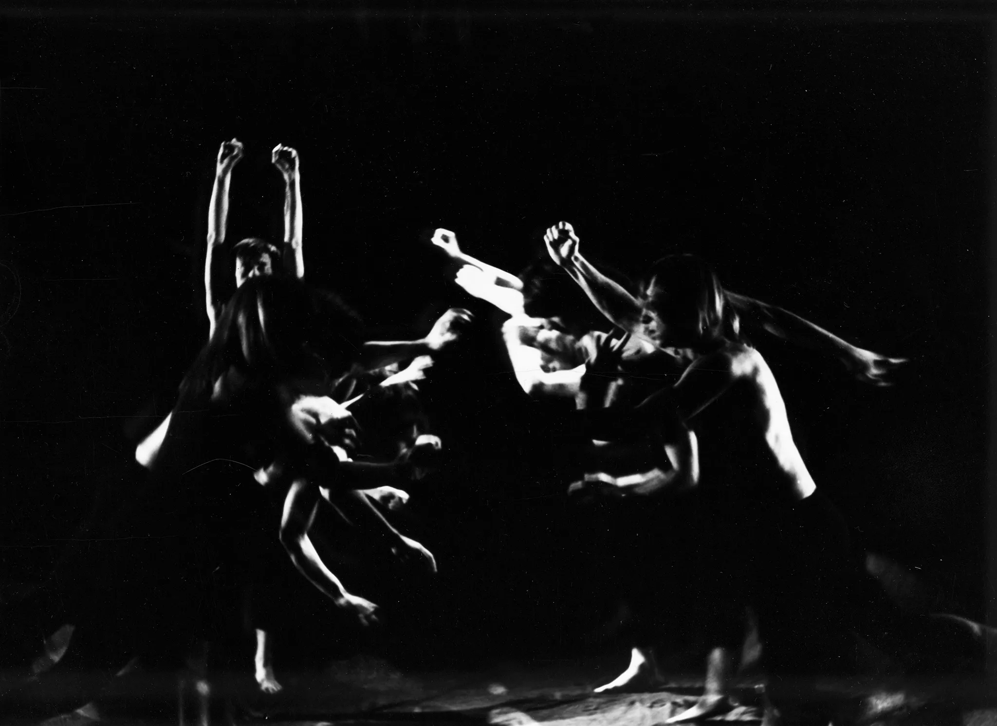 Niewyraźna grupa aktorów bez koszulek w akrobatycznych pozach. Po lewej stronie na podłodze leży kość.