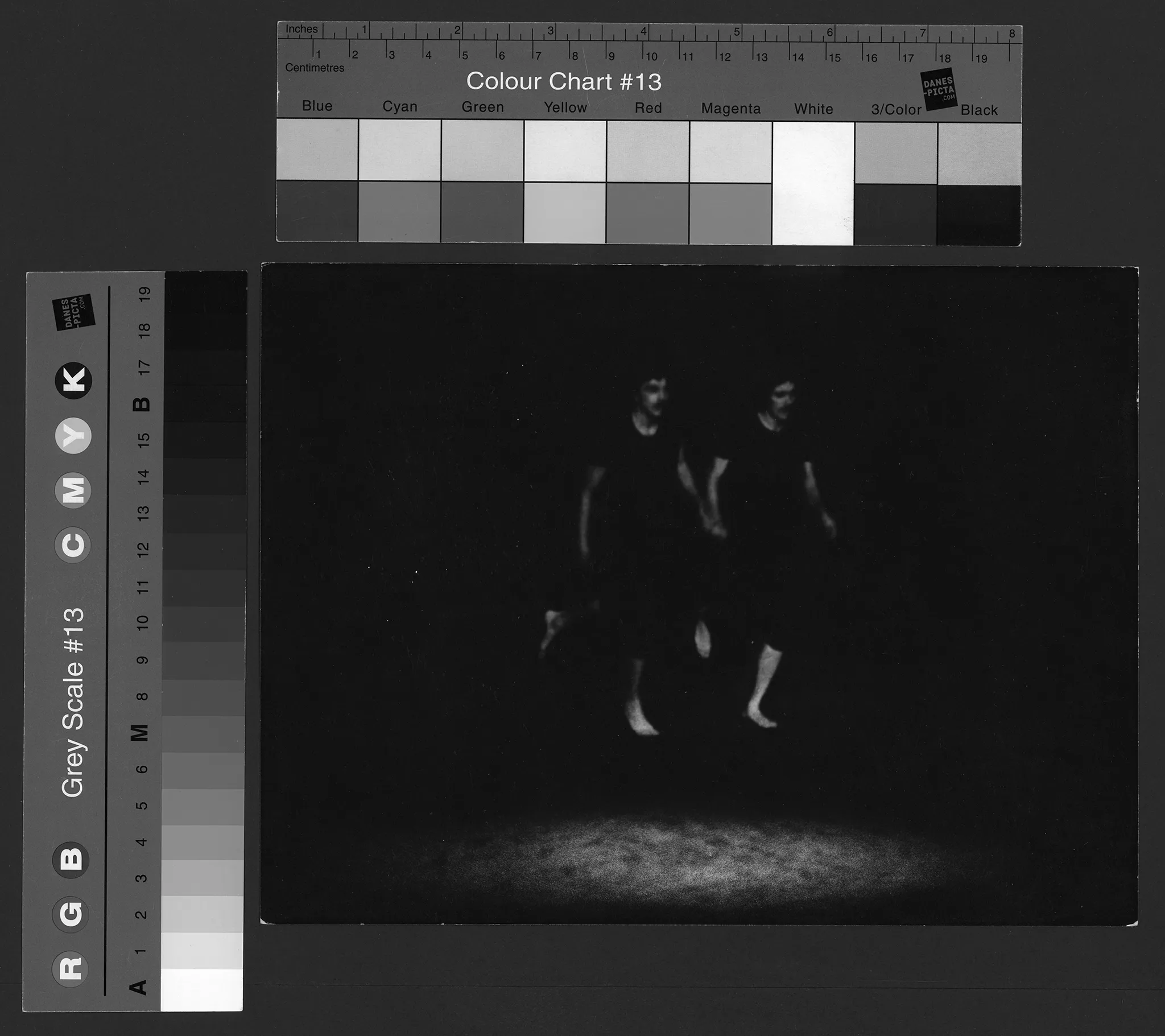 Dwóch aktorów trzyma się za ręce i biegnie przed siebie. Są do siebie bardzo podobni. Mają wąsy, obaj są ubrani w czarne podkoszulki i czarne spodenki. Są bosi.
