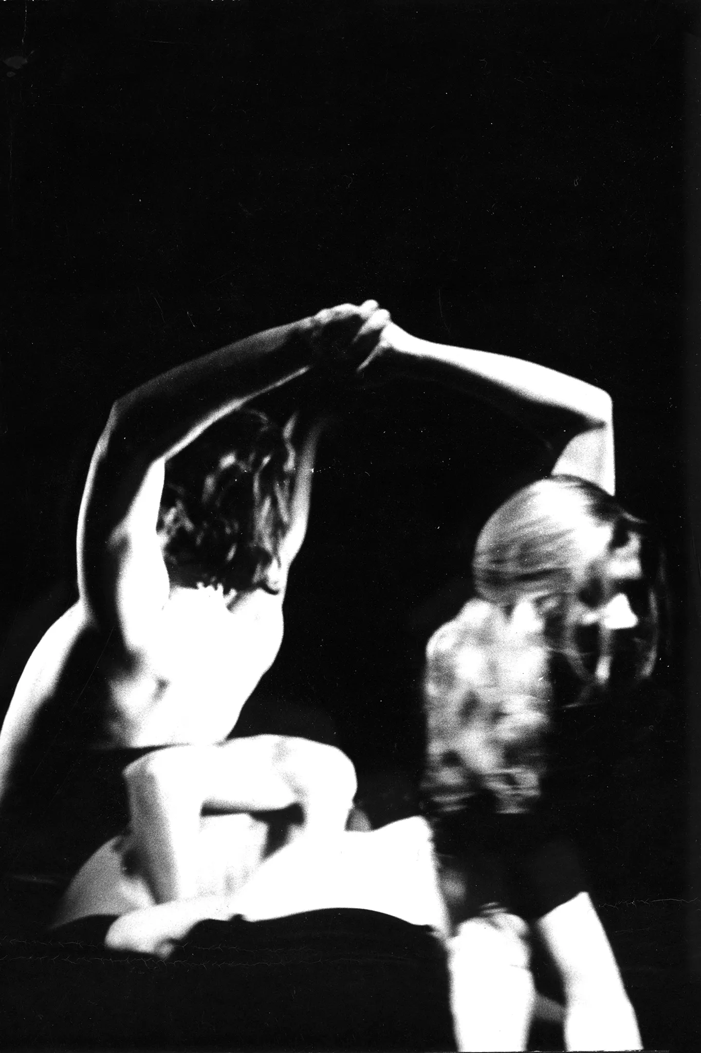 Niewyraźne, rozmazane zdjęcie. Po lewej stronie stoi zwrócony do nas plecami aktor bez koszulki. Ma wyciągnięte za siebie ręce i trzyma w nich rękę aktorki stojącej po prawej stronie. Aktorka wygląda na uśmiechniętą.