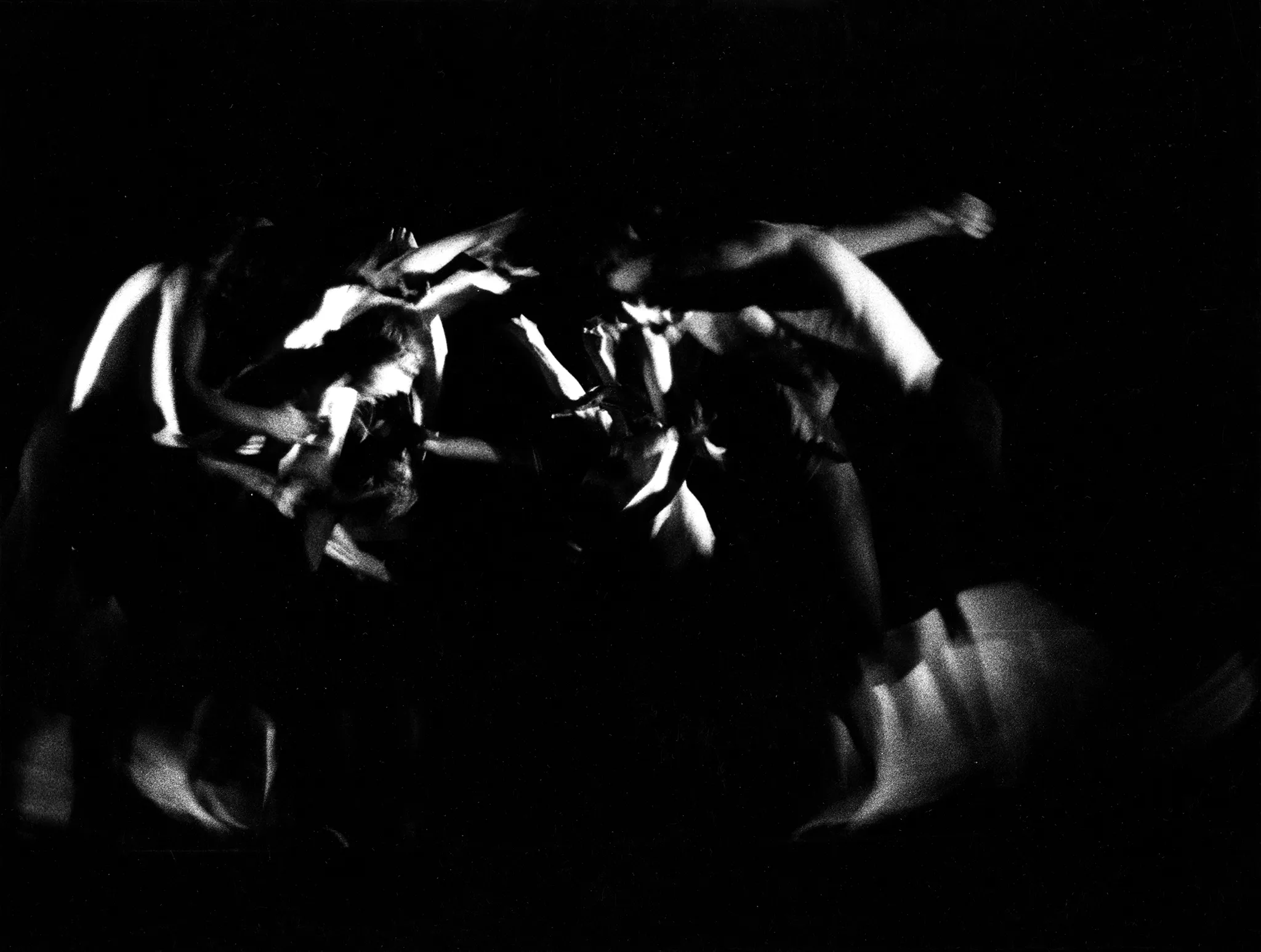 Niewyraźne, rozmazane zdjęcie. Aktorzy stoją po dwóch stronach naprzeciwko siebie w ekspresyjnych pozach. Nie mają na sobie koszulek. Lewa i prawa strona sceny sprawiają wrażenie, jakby przechylały się do środka wraz z aktorami.