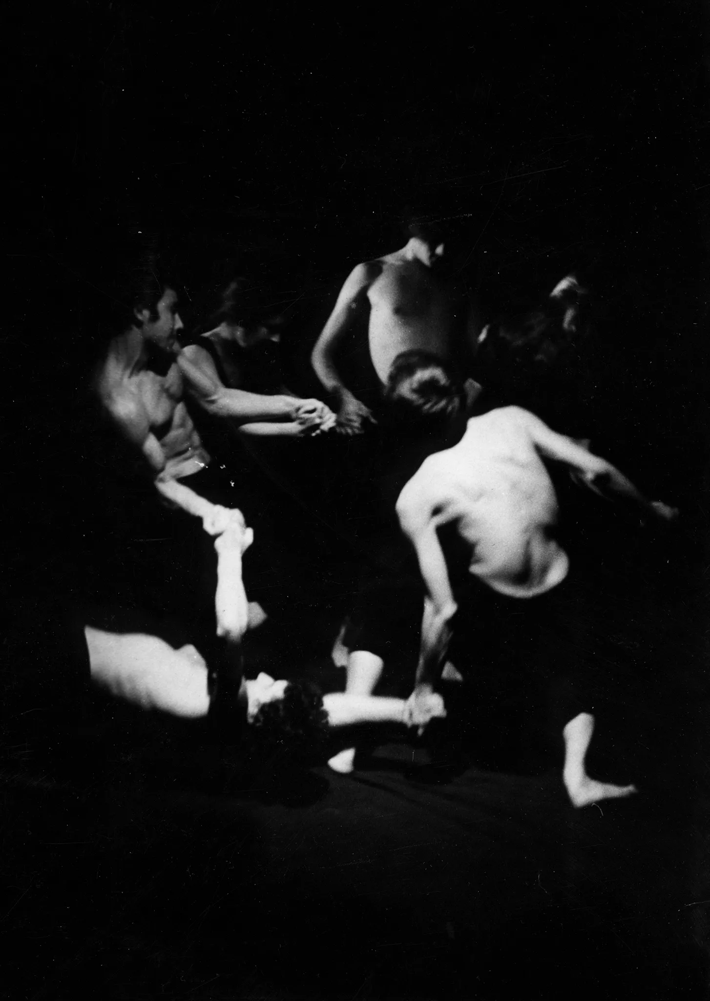 Grupa aktorów stoi w okręgu i trzyma się za ręce. Są ubrani w czarne spodenki, nie mają podkoszulek. Ich wysportowane ciała są napięte.