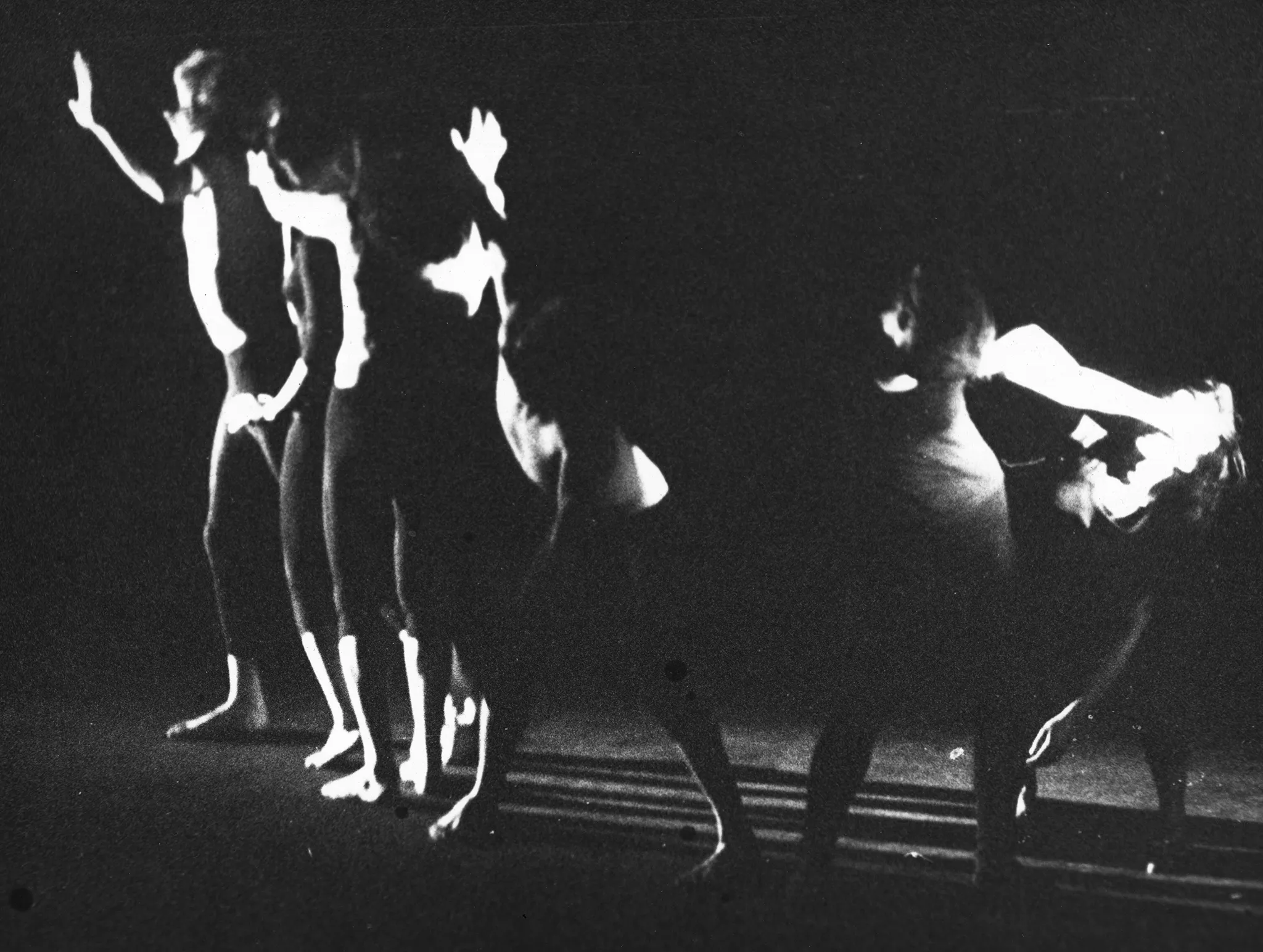 Niewyraźne zdjęcie. Grupa aktorów i aktorek na pustej scenie zmierza w lewą stronę. Dwie aktorki po prawej stronie, odłączone od grupy, wyglądają jakby się biły.