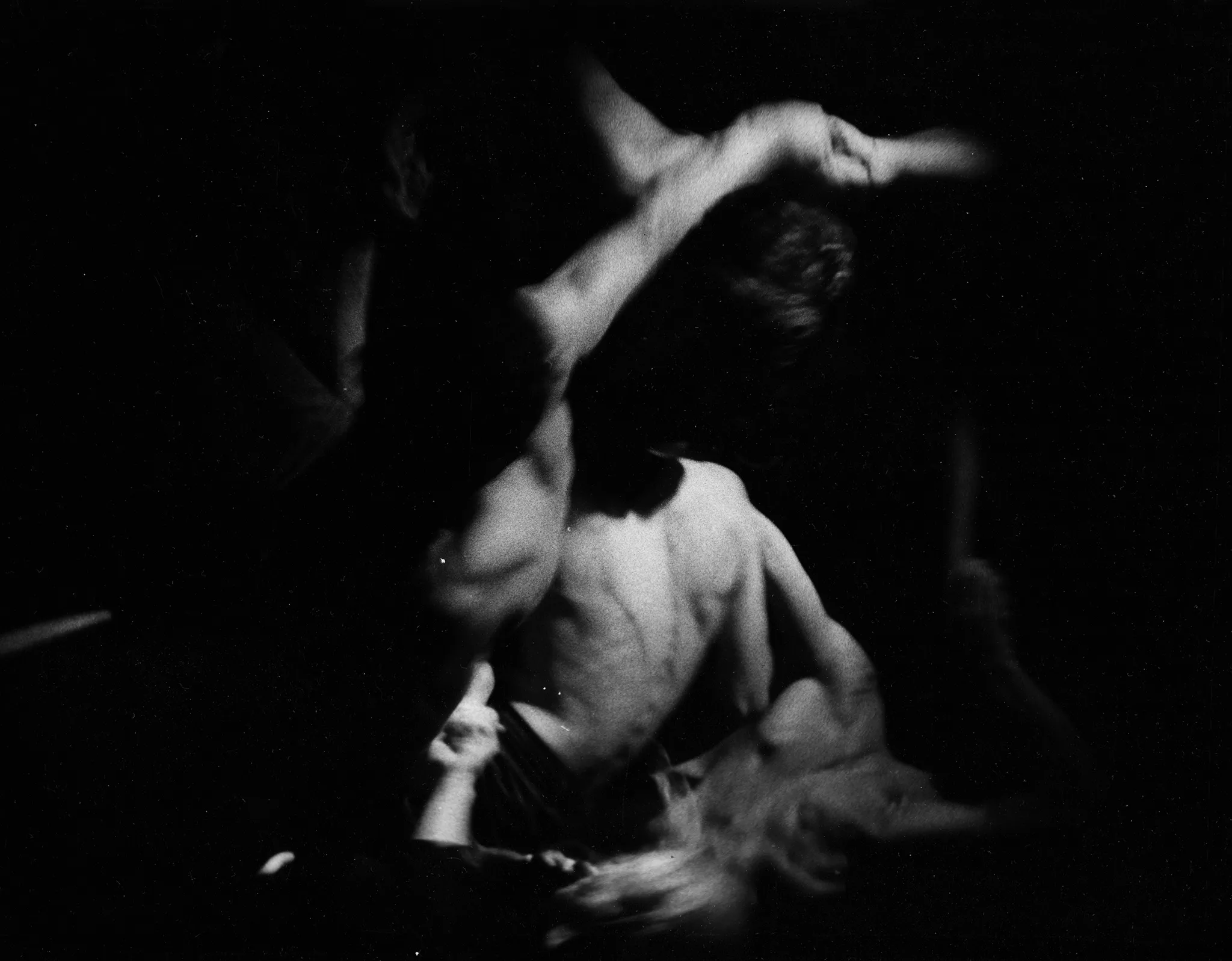 Niewyraźne, rozmazane zdjęcie. Grupa aktorów i aktorek skłębiona na scenie. W centrum aktor zwrócony do nas plecami. Nie ma na sobie koszulki.