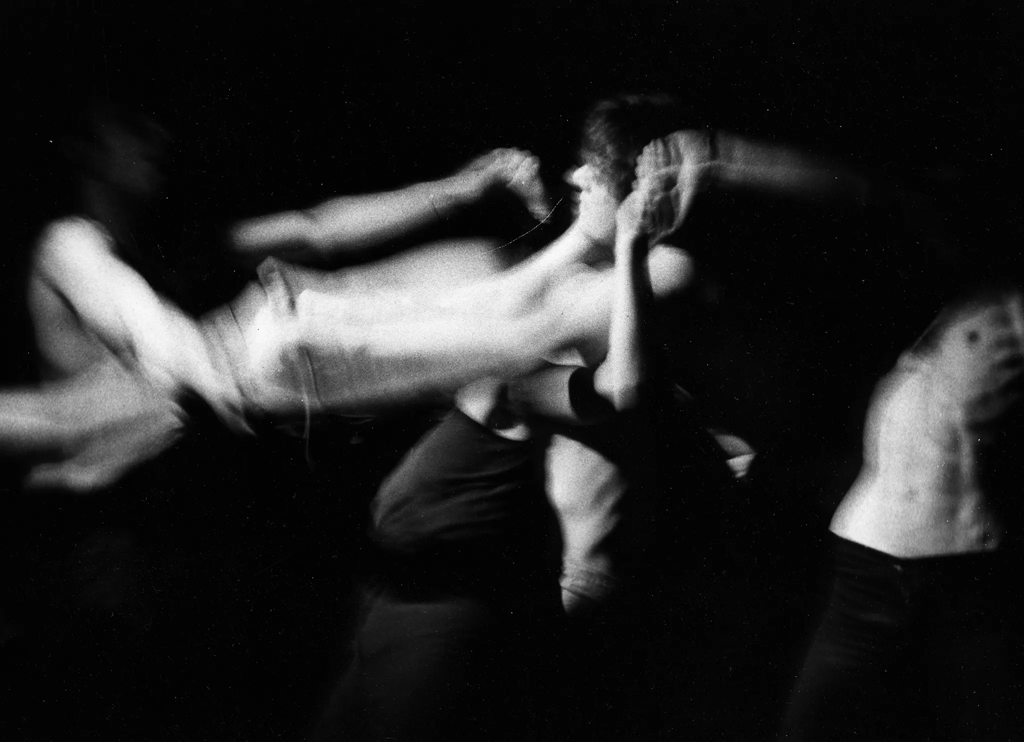 Niewyraźne, rozmazane zdjęcie. Aktor stojący w centrum wygląda, jakby ktoś wisiał na jego szyi. Po prawej stronie z cienia wyłania się wysportowany tors aktora.