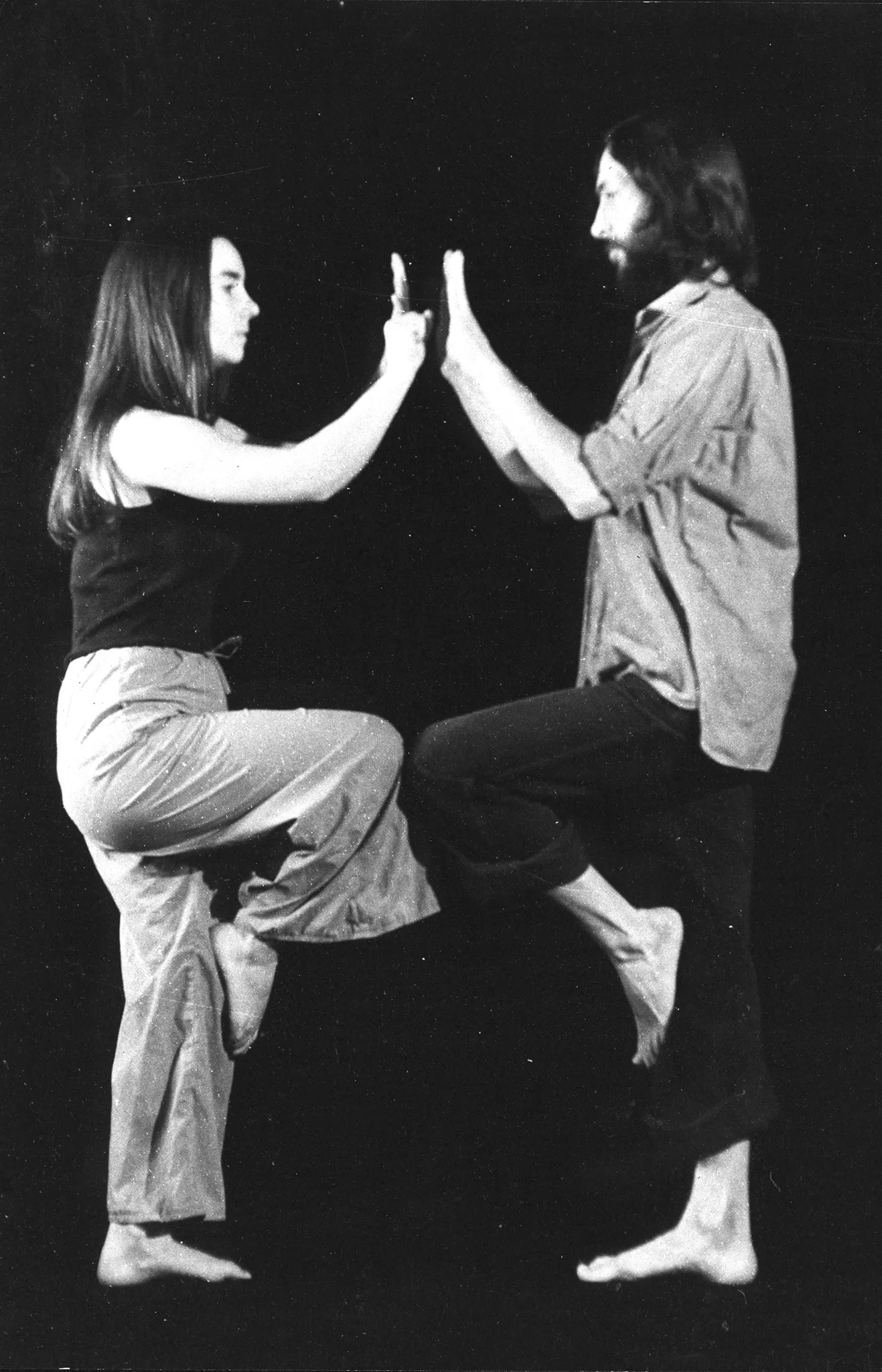 Naprzeciwko siebie stoją zwróceni profilem do widzów aktor i aktorka. Aktorka stoi z lewej strony, aktor - z prawej. Aktorka ubrana jest w jasne spodnie i czarną podkoszulkę. Aktor ubrany jest w czarne spodnie i jasną koszulę. Oboje są boso. Stoją na jednej nodze, drugą nogę trzymają ugiętą w górze. Stykają się uniesionymi nogami. Ręce mają wyciągnięte przed siebie i prawie się nimi dotykają.