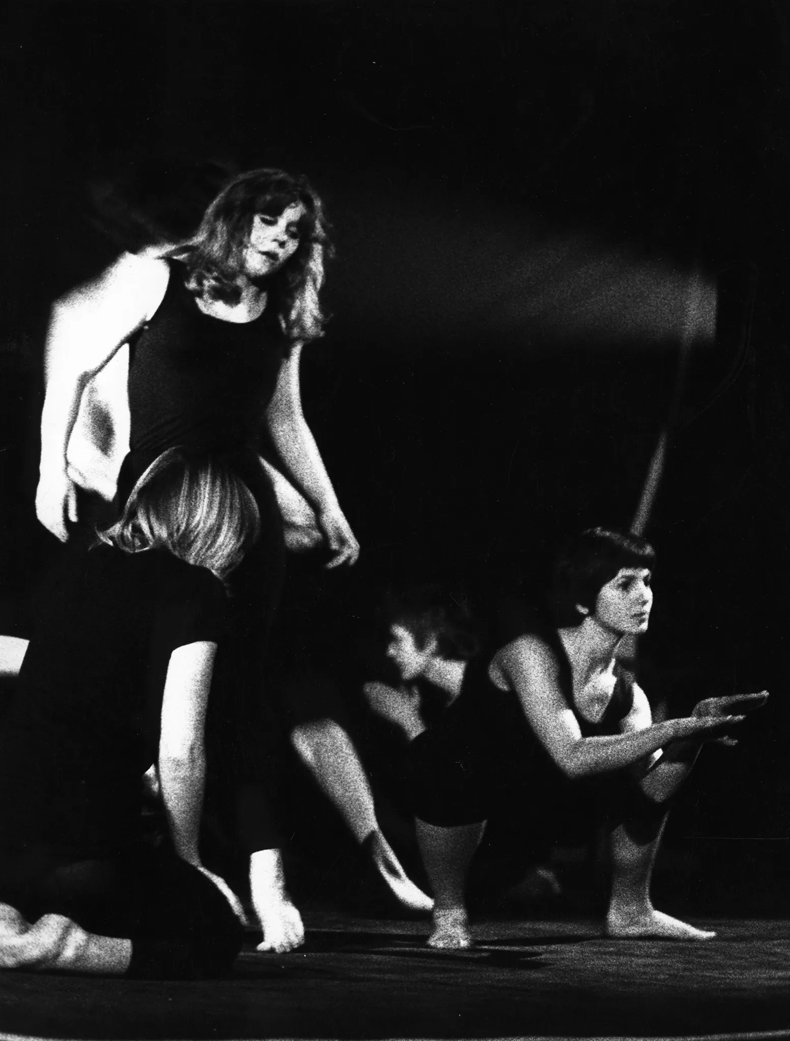 Po lewej stronie, zwrócona tyłem do widza, klęczy aktorka. Obok niej, zwrócona przodem do widza, stoi druga aktorka, która patrzy na nią z góry. Po prawej stronie, zwrócona przodem do widza, kuca aktorka patrząca w stronę widowni. Wszystkie ubrane są w czarne spodenki i czarne podkoszulki. W tle ledwo wyraźny aktor zwrócony do widza profilem.