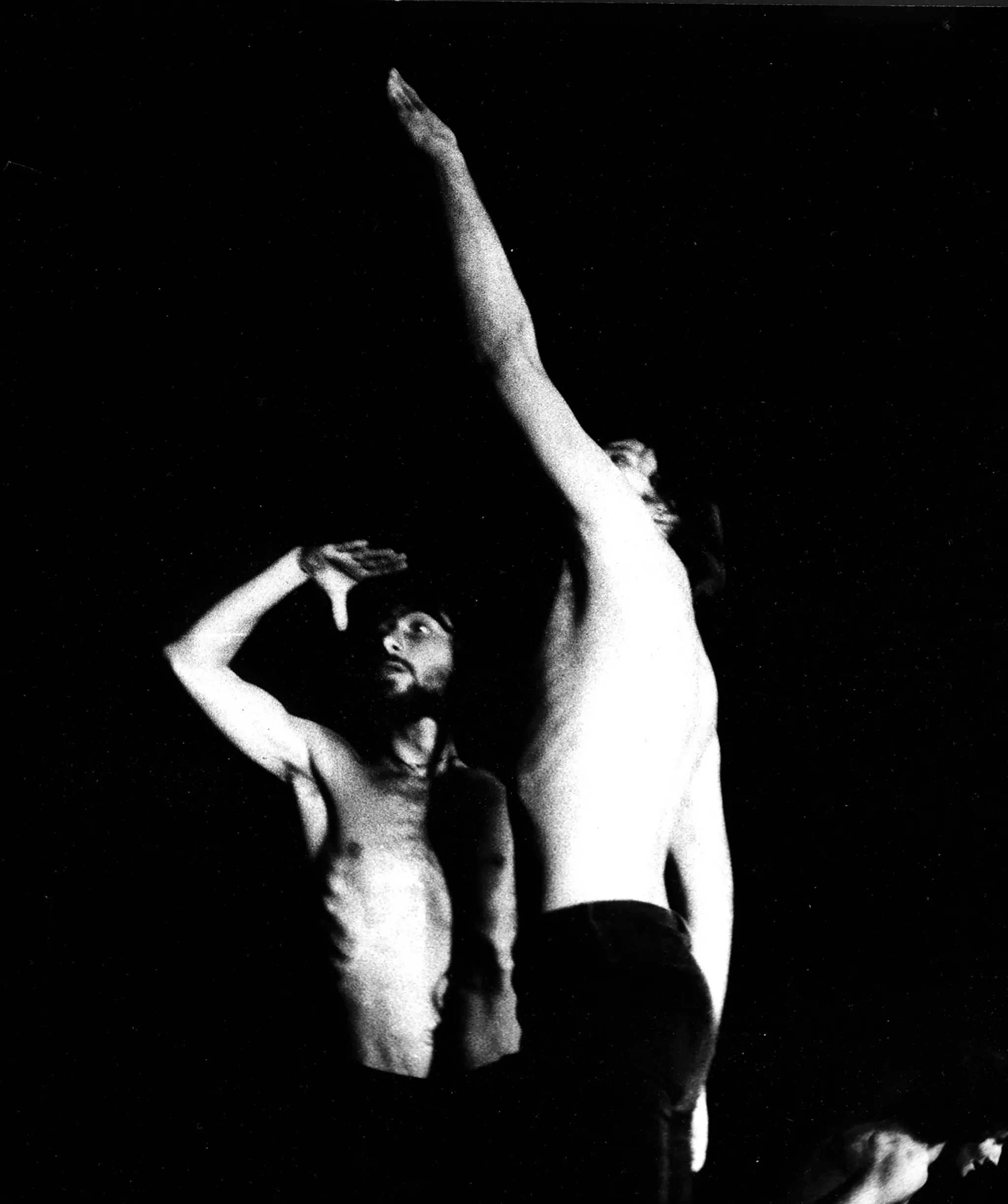 Dwóch aktorów stoi blisko siebie. Obaj mają nagie torsy. Patrzą w dal. Aktor z lewej strony ma lekko uniesioną, zgiętą rękę. Aktor z prawej strony ma rękę wyprostowaną, uniesioną wysoko w górze.