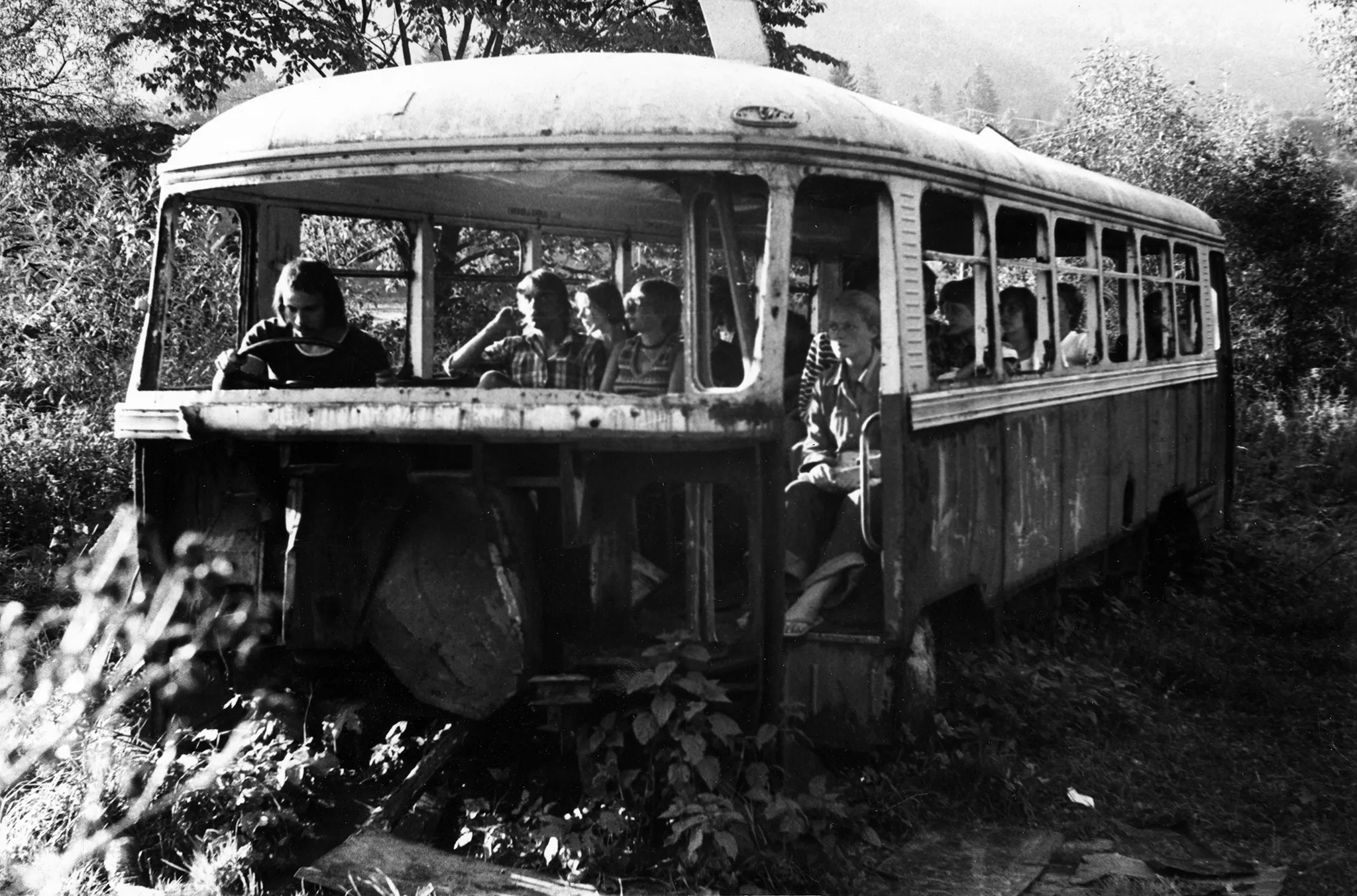 Stary, zniszczony autobus w środku lasu. W środku autobusu siedzą aktorzy. Ubrani są prywatnie, wyglądają jakby byli pasażerami.