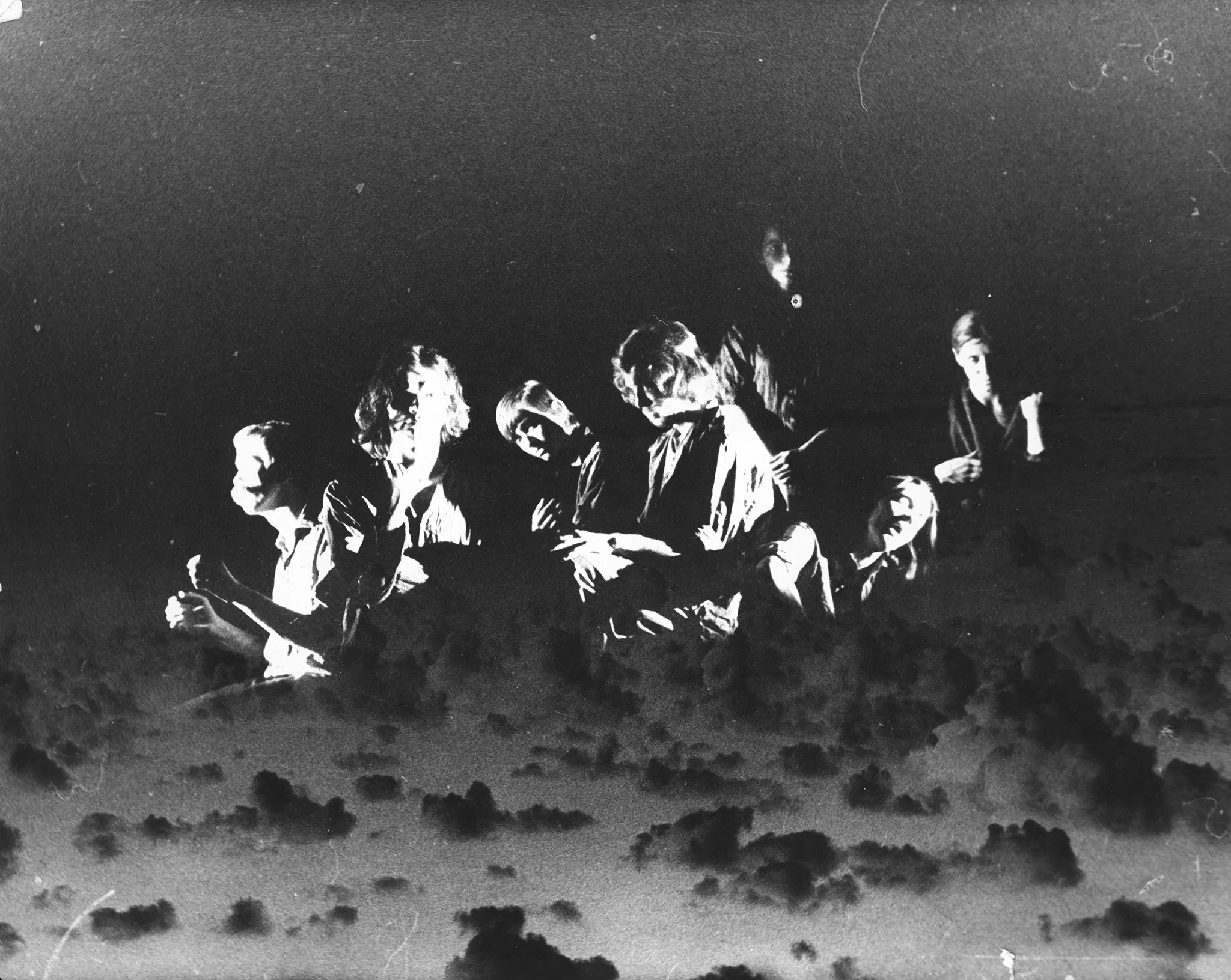 Niewyraźne zdjęcie. Wygląda jak montaż dwóch zdjęć. Grupa aktorów i aktorek. Wyglądają, jakby siedzieli w autobusie, który unosi się nad chmurami.