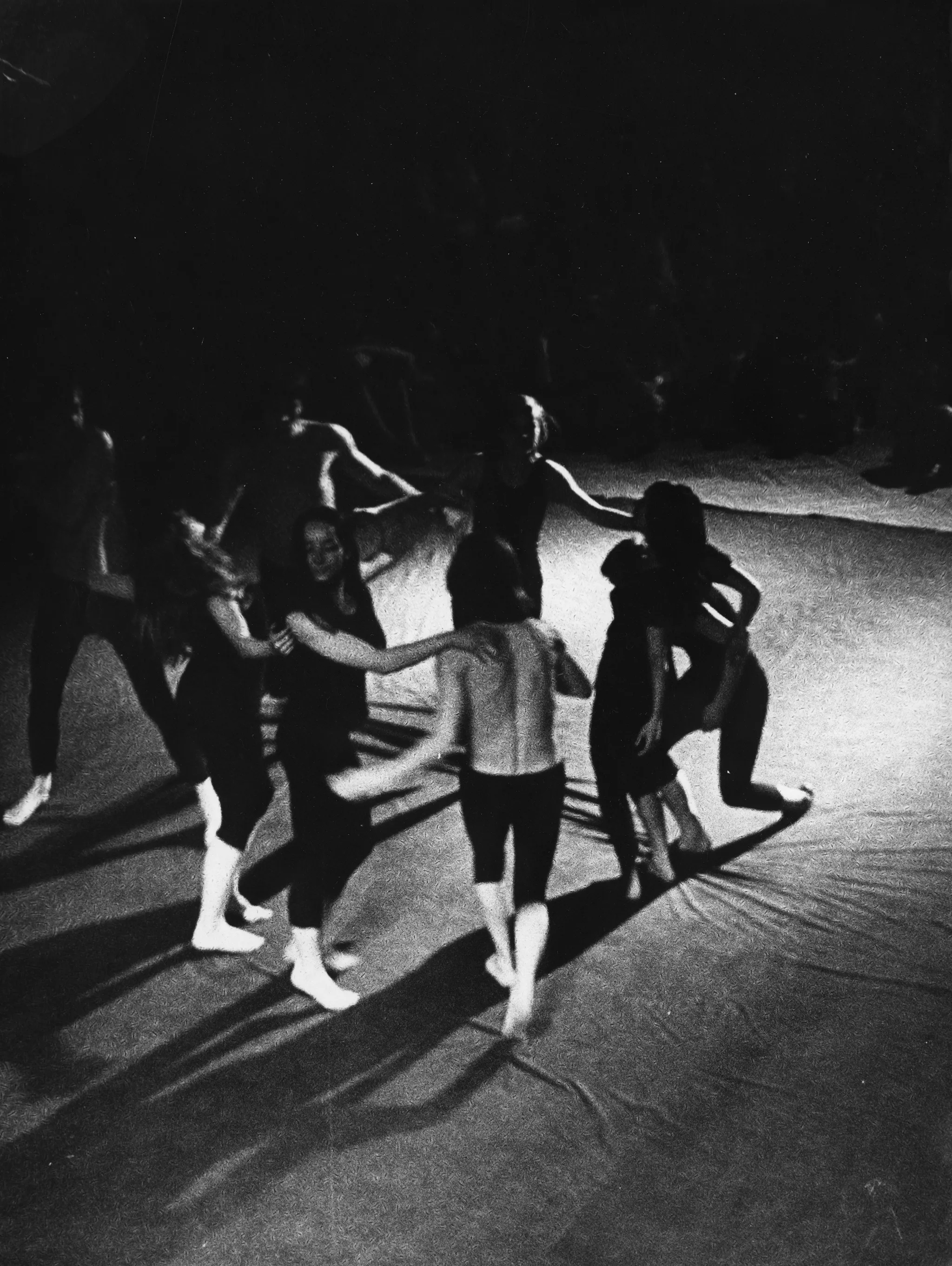 Scena wyglądająca jak wyłożona prześcieradłem. Na scenie grupa aktorów i aktorek widzianych od góry.Stoją w okręgu i wyglądają, jakby tańczyli. Aktorzy ubrani są w ciemne spodenki, mają nagie torsy. Aktorki ubrane są w czarne spodenki i czarne podkoszulki. Na drugim planie siedząca grupa widzów.