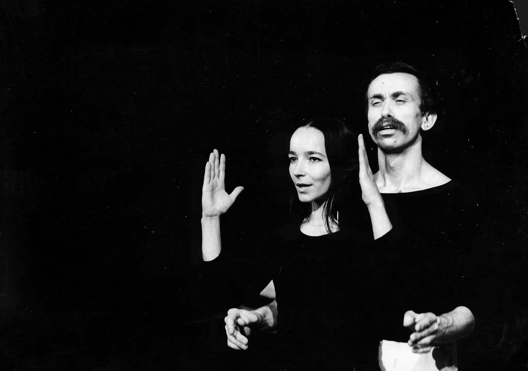 Aktor i aktorka stoją zwróceni twarzą w stronę widza. Widać ich od pasa w górę. Aktorka ma lekko uniesione ręce. Aktor stoi tuż za nią i wygląda, jakby chciał objąć aktorkę. Aktorka się uśmiecha. Aktor ma zbolały wyraz twarzy. Oboje ubrani są na czarno.