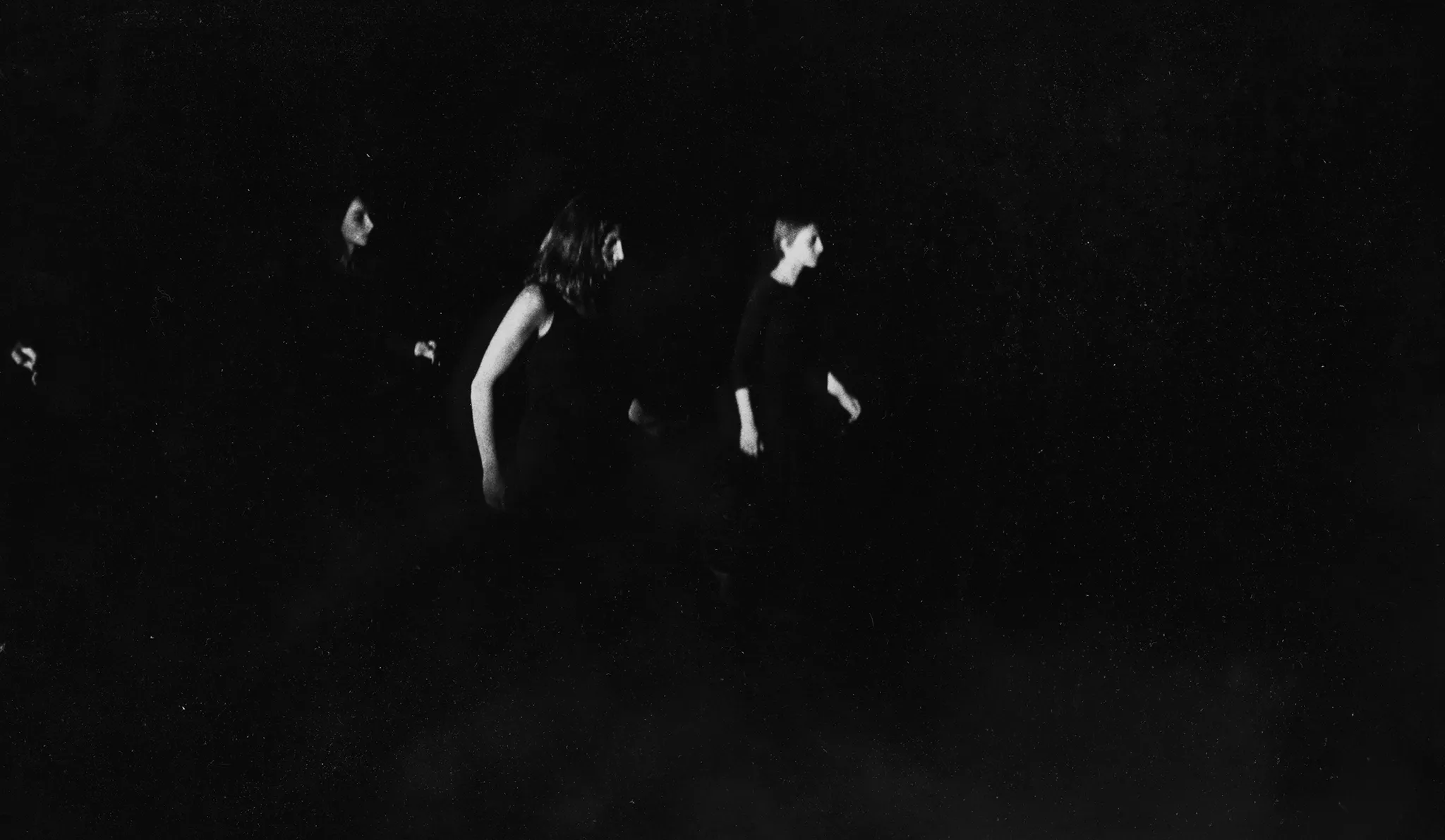 Niewyraźne zdjęcie. Z cienia wyłania się grupa aktorek stojących profilem w stronę widza. Aktorki ubrane są na czarno.