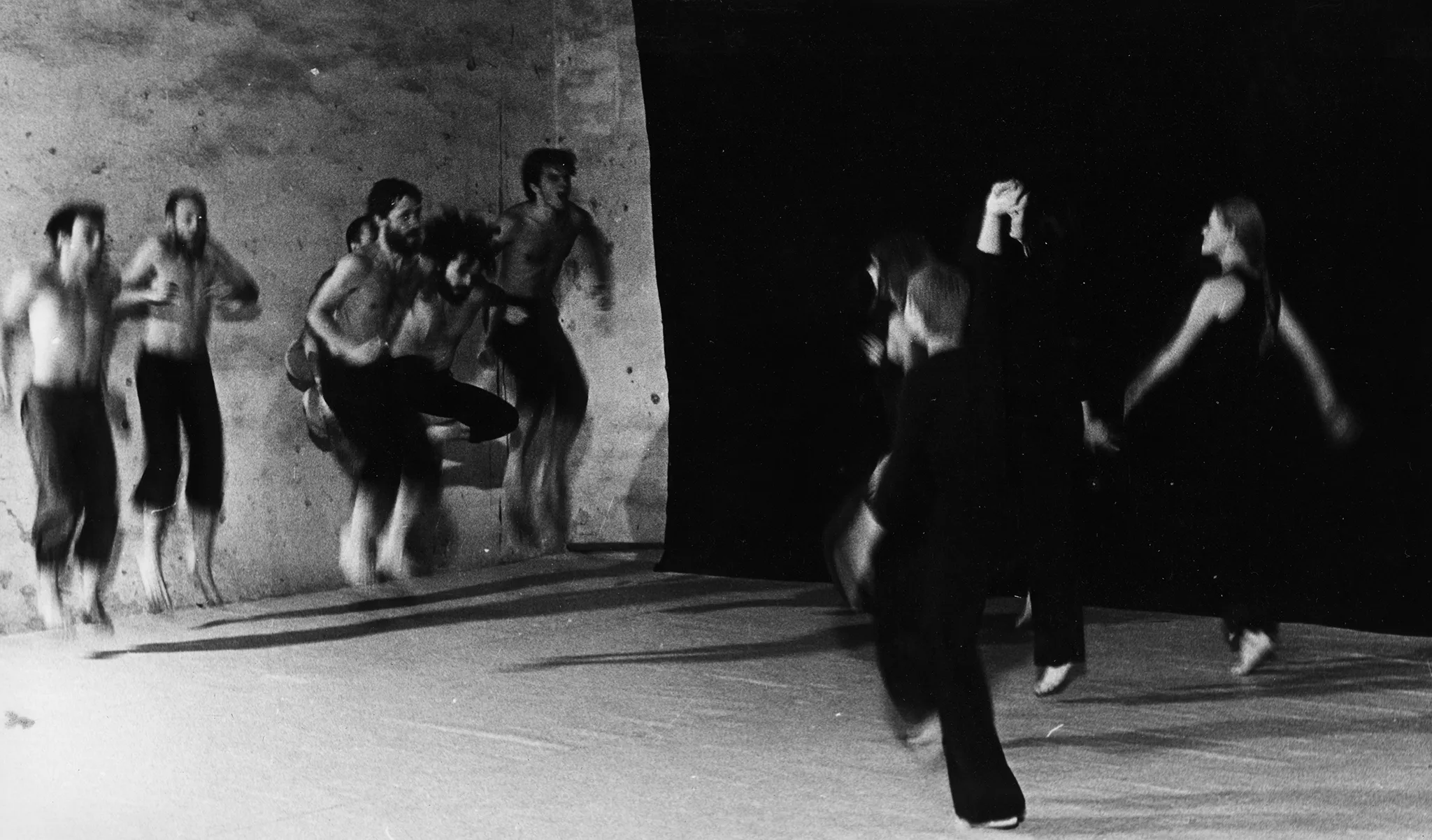 Po dwóch stronach sceny, na tle czarnej płachty, stoją aktorzy i aktorki. Aktorzy po lewej stronie, aktorki po prawej. Obie grupy są zwrócone w swoją stronę. Aktorzy ubrani są w czarne spodenki, mają nagie torsy. Aktorki ubrane są w czarne spodnie i czarne koszulki. Obie grupy podskakują.