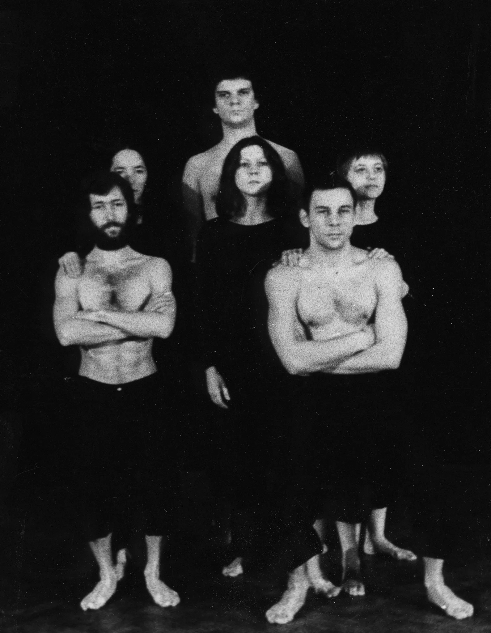 Grupa aktorów i aktorek stojących twarzą w stronę widza. Wyglądają, jakby pozowali do zdjęcia. Dwóch aktorów z przodu napina mięśnie. Ubrani są w czarne spodenki i mają nagie torsy. Za nimi stoją trzy aktorki ubrane na czarno. Z tyłu stoi bardzo wysoki aktor.