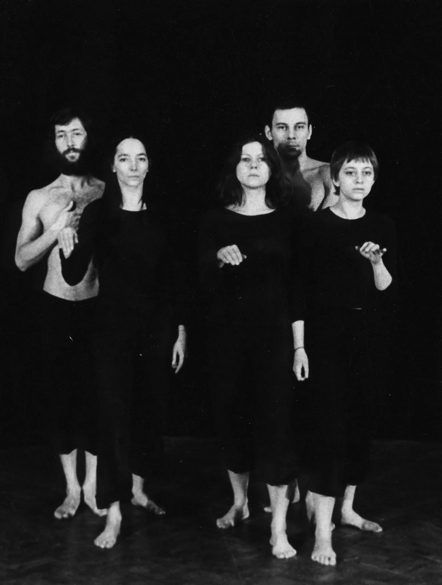 Dwóch aktorów i trzy aktorki stoją twarzą w stronę widza. Aktorki ubrane są na czarno. Aktorzy stoją za ich plecami. Mają nagie torsy. Wszyscy są boso.