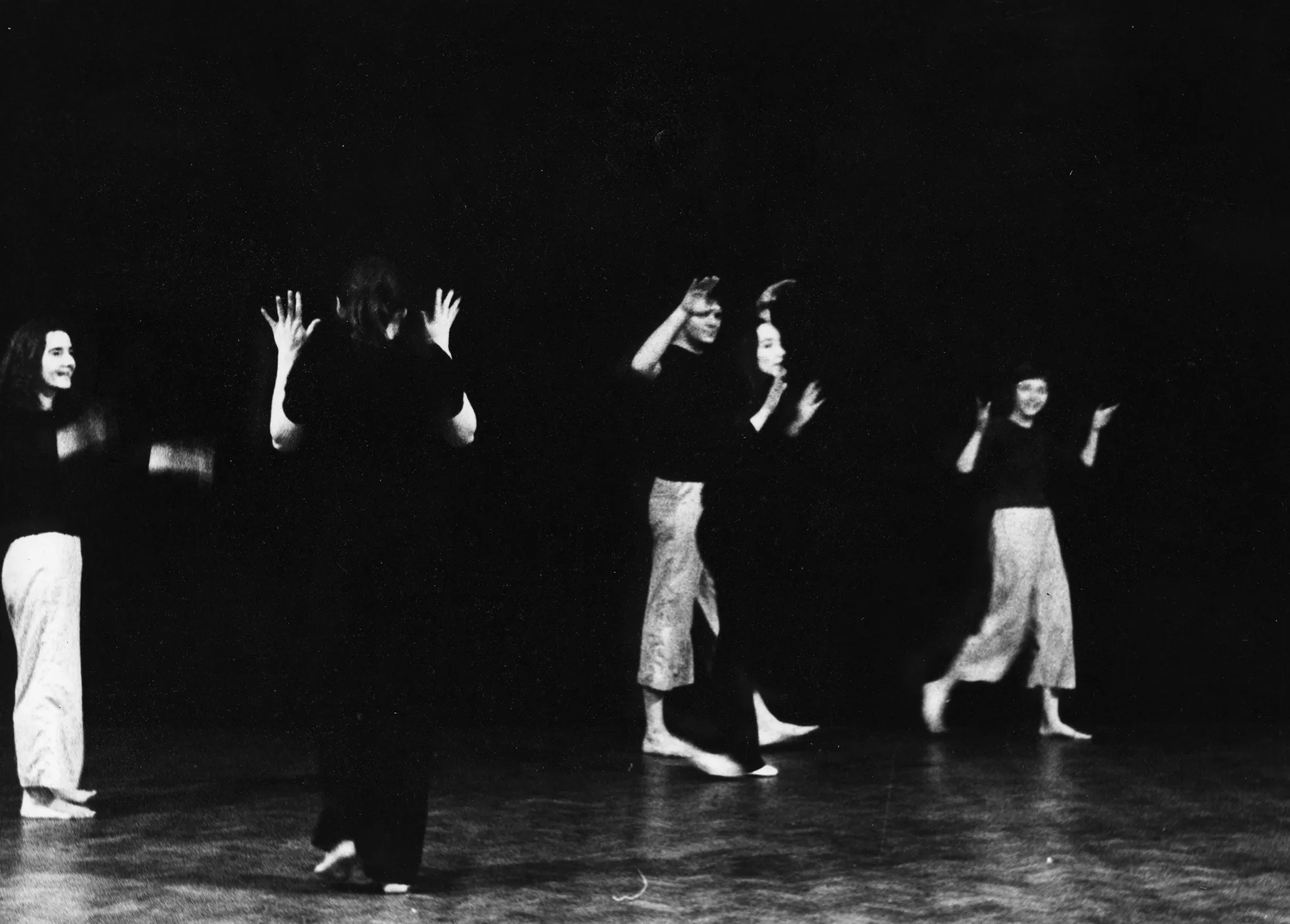 Jeden aktor i cztery aktorki chodzą po scenie. Mają lekko uniesione ręce i uśmiechają się. Aktor i dwie aktorki ubrani są w jasne spodnie i czarne koszulki. Dwie aktorki ubrane są w czarne spodnie i czarne koszulki. Wszyscy sa boso.