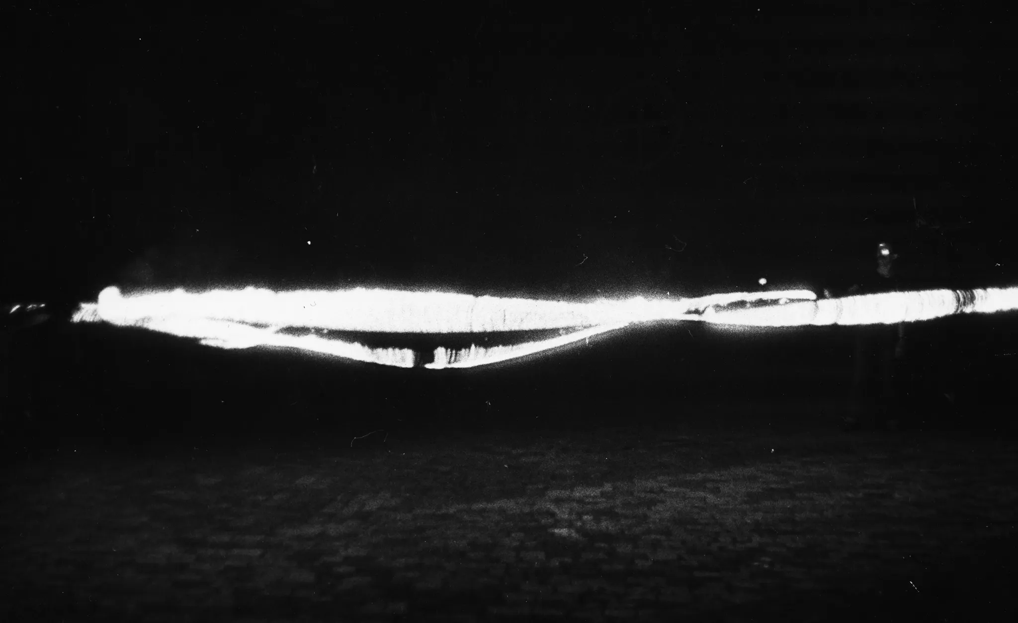 Niewyraźne zdjęcie. Na brukowanej ulicy stoją aktorzy. Trzymają przedmioty emitujące silne światło.